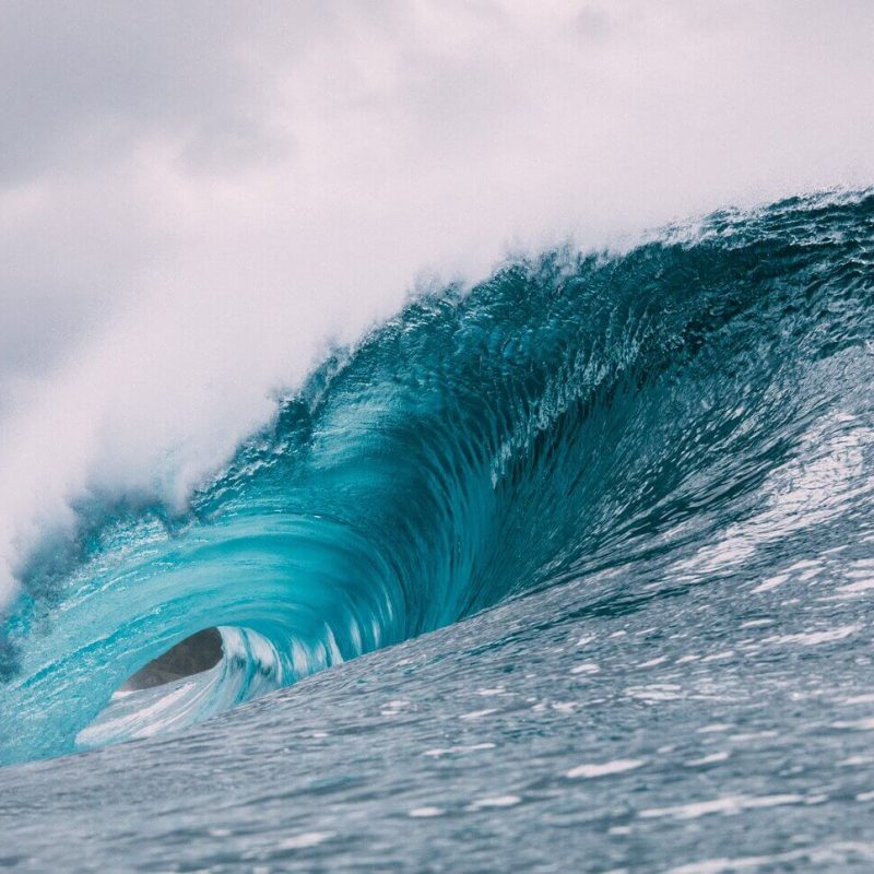 A blue ocean wave crashing against a grey sky